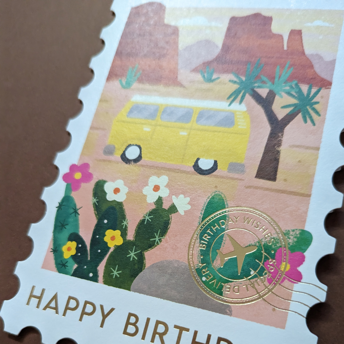 Carte d'anniversaire ornée d'un camping-car de style vintage dans le parc national de Joshua Tree, ce design élégant est découpé à l'emporte-pièce en forme de timbre et orné d'un cachet de la poste doré et de l’inscription Happy Birthday.