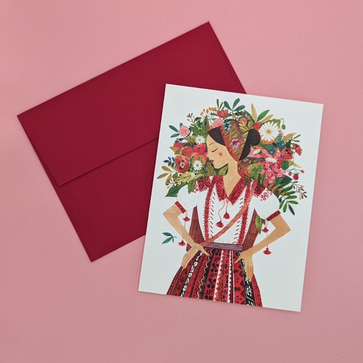 Une jeune roumaine vêtue d'une tenue traditionnelle, porte à son dos un panier rempli de jolies fleurs. Cette carte évoque la beauté, la nature et la tradition.