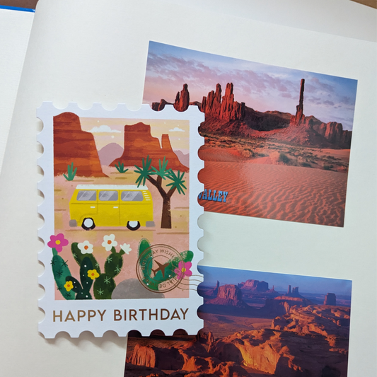 Carte d'anniversaire ornée d'un camping-car de style vintage dans le parc national de Joshua Tree, ce design élégant est découpé à l'emporte-pièce en forme de timbre et orné d'un cachet de la poste doré et de l’inscription Happy Birthday.