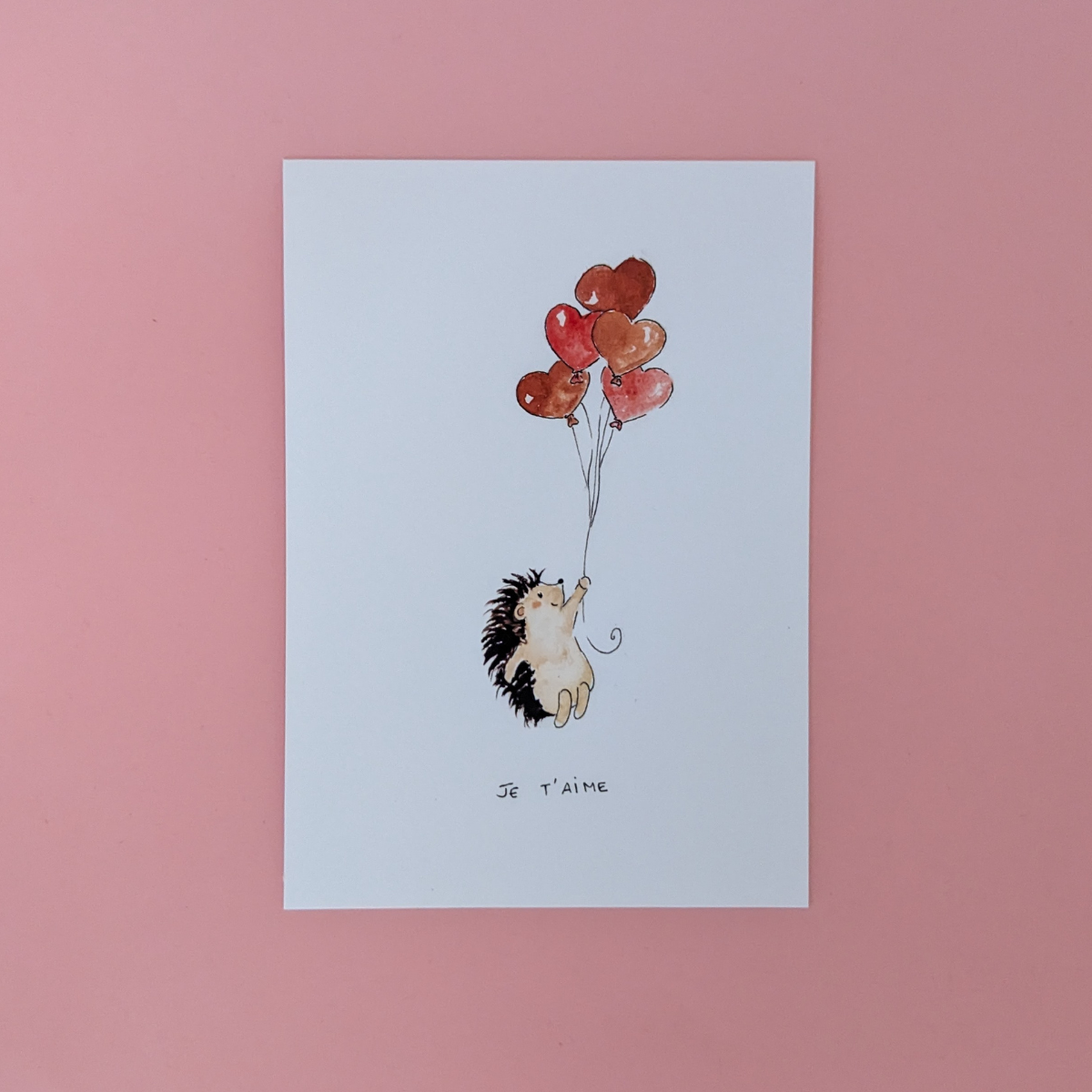 Illustration d'un hérisson qui s'envole avec des ballons en forme de coeur pour dire à une personne qui vous est chère que vous l'aimez. Vous pouvez écrire votre message au dos de la carte.