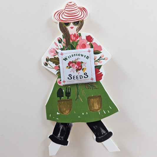 Cette jolie jardinière tient dans ses bras un magnifique bouquet de fleurs aux teintes délicates de rose avec un véritable petit sachet de graines de fleurs sauvages offrant ainsi à votre destinataire la possibilité de les planter dans son jardin ou en pot. Imaginez la joie qu'apportera une telle carte.
