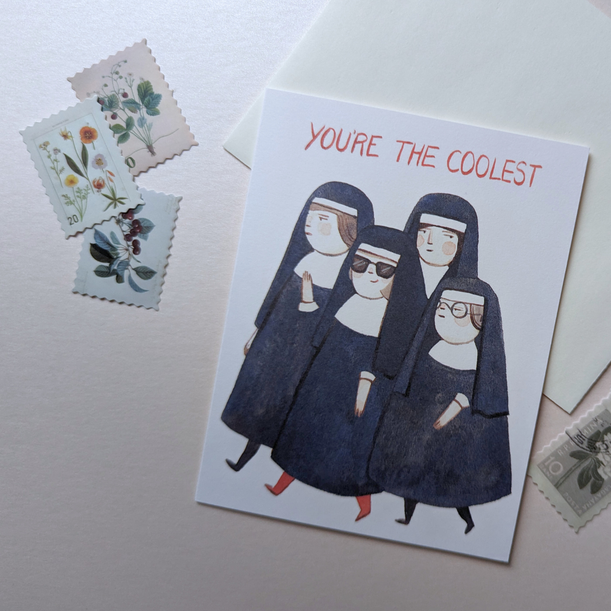 La carte met en scène un groupe de religieuses austères. Parmi elles, une nonne se démarque en arborant des lunettes de soleil, des bas rouges et un grand sourire.