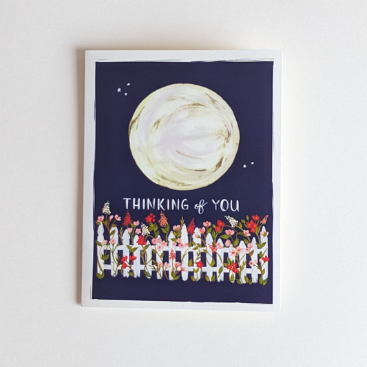 Carte réalisée par The First Snow. L'illustration d'une lune majestueuse, d'une clôture de jardin très fleurie et ces mots " thinking of you " donneront le sourire à votre destinataire. À l'intérieur de la carte vous pouvez laisser votre message.