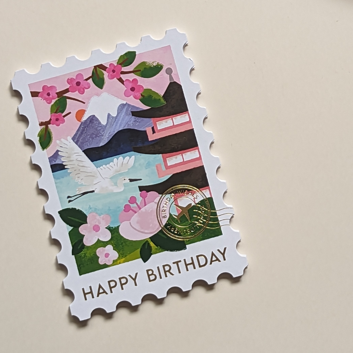 Cette carte en forme de timbre arbore une superbe illustration du Mont Fuji. Le cachet doré de la poste affiche les mots « Birthday Wishes », ce qui ajoute une touche d’authenticité.