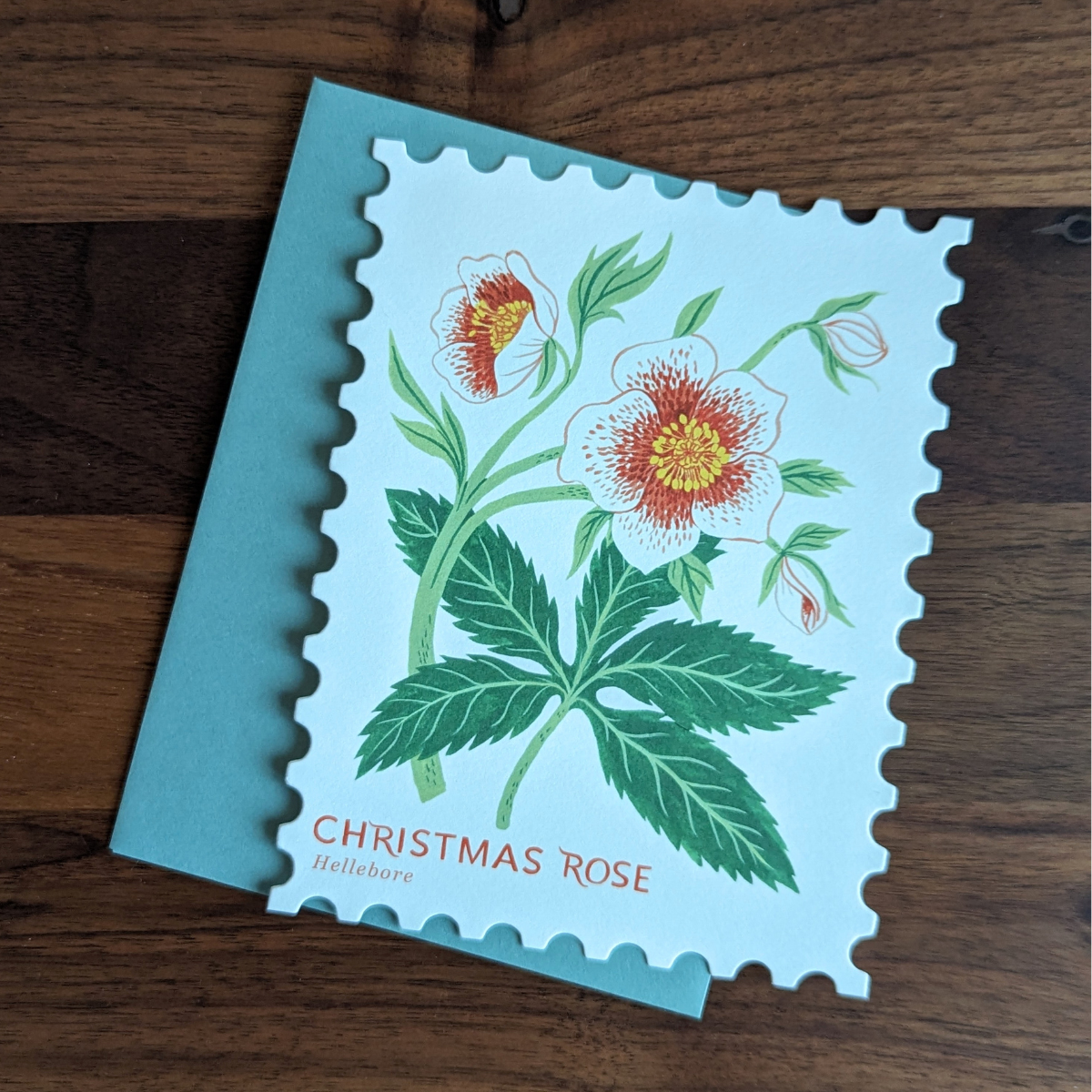 Carte de Noël découpée en forme de timbre. Sur le devant de la carte l'illustration d'une très belle rose de Noël a été réalisée par Botanica Paper Co. 