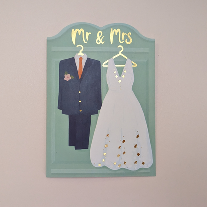 Avec un costume bleu marine pour le marié, une robe de mariée en dentelle blanche avec des détails dorés et une inscription « Mr & Mrs » finie dans une feuille d'or de luxe, c'est une carte vraiment digne de célébrer une belle journée. et d'envoyer vos vœux de mariage.