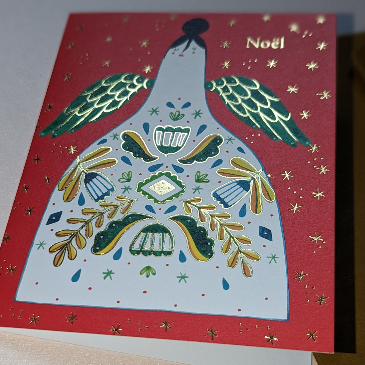 Carte de Noël Halfpenny Postage. On peut voir un ange avec de la dorure sur ses ailes et sur les éléments qui ornent sa robe. L’inscription " Noël " est en dorure rendant l'ensemble très scintillant.