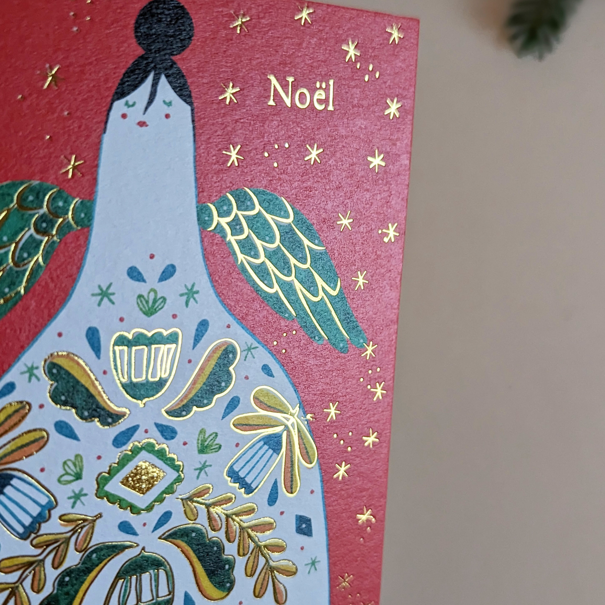 Carte de Noël Halfpenny Postage. On peut voir un ange avec de la dorure sur ses ailes et sur les éléments qui ornent sa robe. L’inscription " Noël " est en dorure rendant l'ensemble très scintillant.