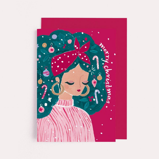 Carte Merry Christmas avec l’illustration  d'une jeune fille dont les cheveux sont joliment décorés de sucres d’orge, de boules de Noël et de houx créant un look festif et amusant .