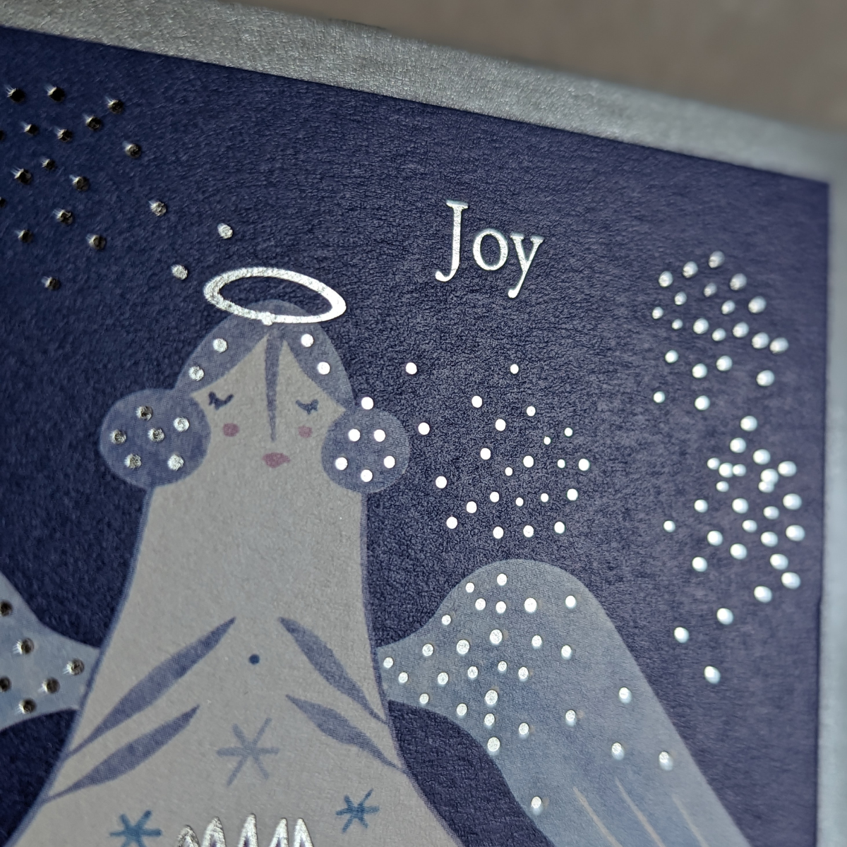 Carte de Noël ornée d'un ange bleu avec des touches argentées et l'inscription " joy ".