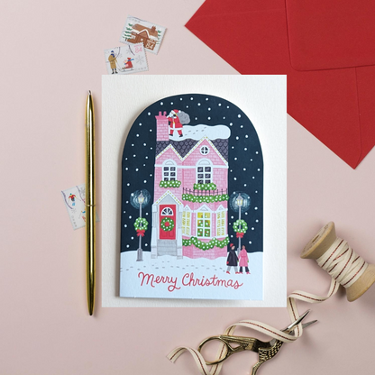 La maison rose joliment décorée et le Père Noël près de la cheminée créent une image qui évoque instantanément la féerie des fêtes.