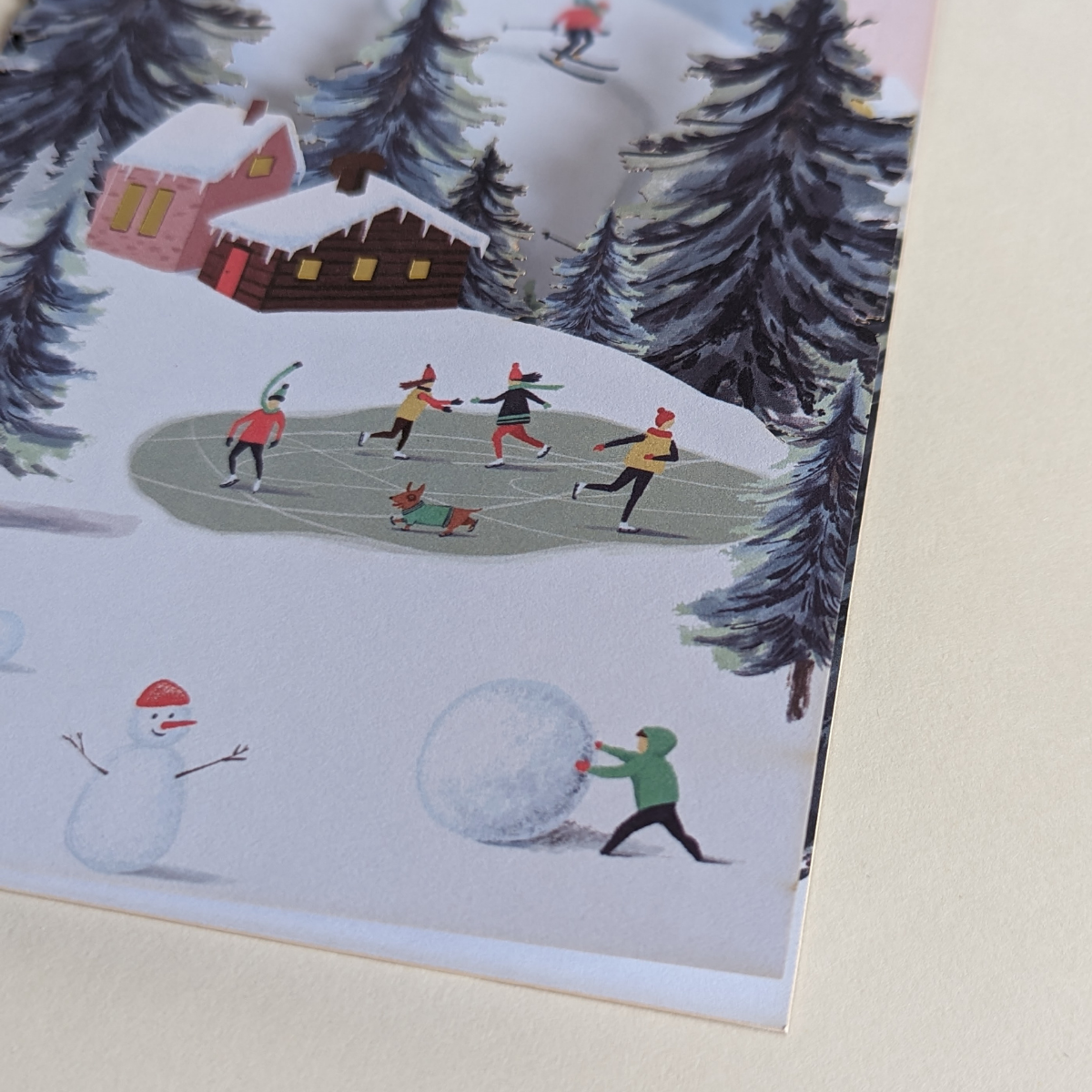 Carte d'hiver découpée au laser.Des chalets dans la montagne, une forêt de sapins, des personnes faisant du patinage ont été représentées sur cette très belle carte de voeux.