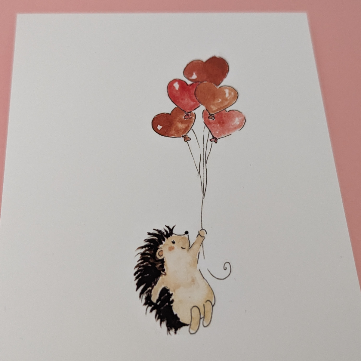 Illustration d'un hérisson qui s'envole avec des ballons en forme de coeur pour dire à une personne qui vous est chère que vous l'aimez. Vous pouvez écrire votre message au dos de la carte.