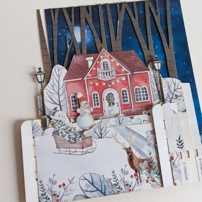Cette carte en 3D pop-up présente une scène hivernale avec une charmante maison nichée au cœur d'une forêt enneigée. 