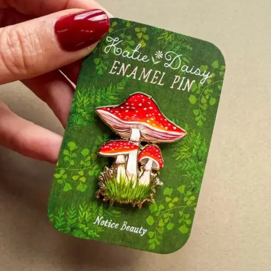 Pin’s émaillé Katie Daisy représentant trois champignons rouges à pois blancs dans l’herbe.